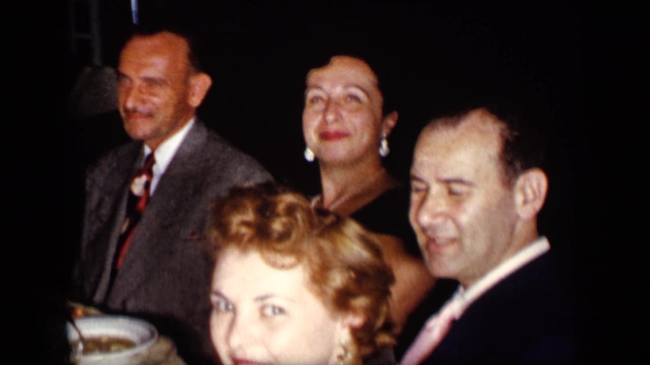 Adults in formal clothes seated closely at a dim dinner table.