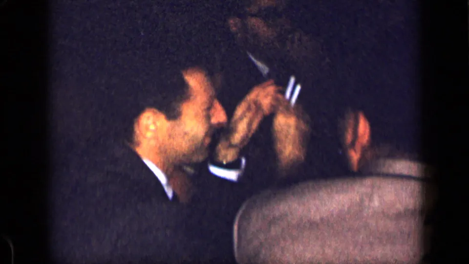 1957 New York 8mm frame showing a suited man in profile at a dark candlelit dinner table with adults around him.