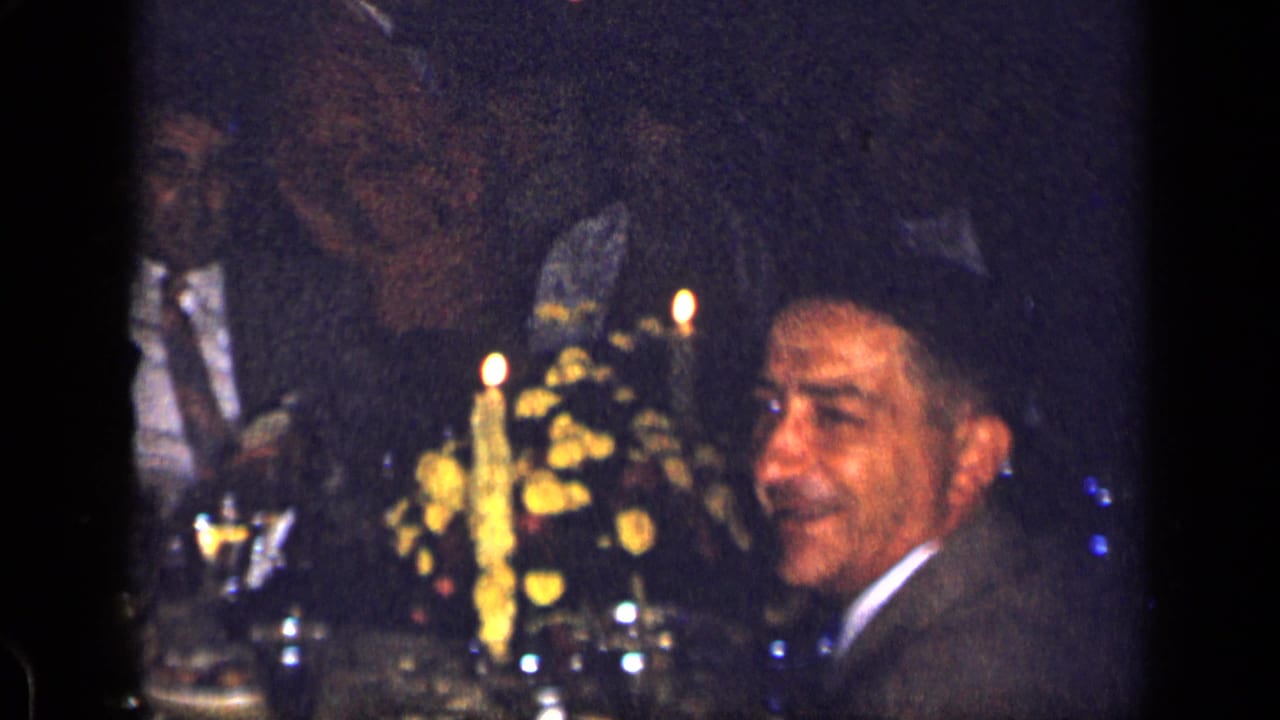A suited diner turns toward the camera during a 1957 New York restaurant dinner, with candles and flowers on the table.