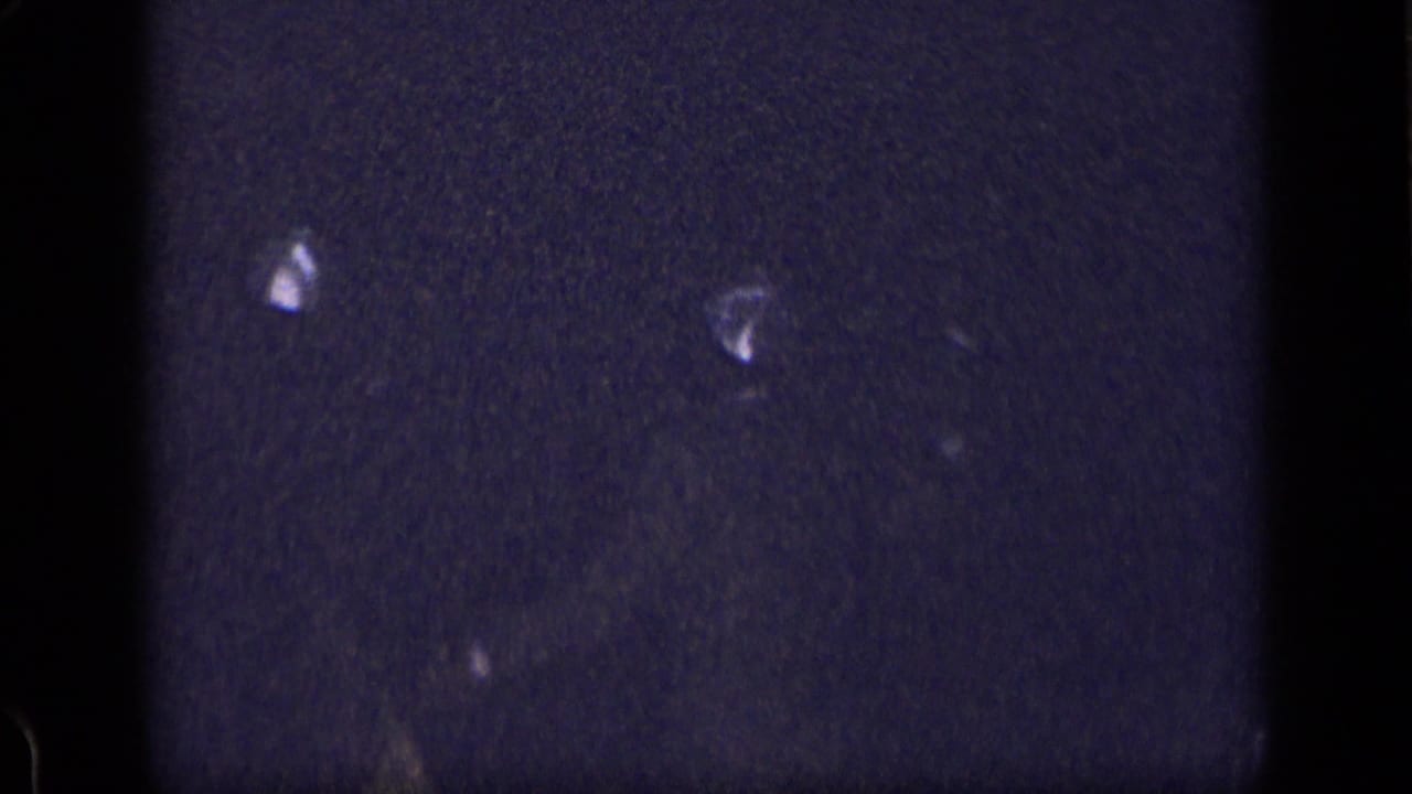 Dark underexposed frame with small bright fragments and visible film grain.