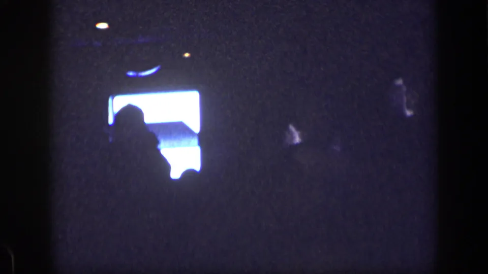Dark 8mm frame showing a bright rectangular light area and silhouette, with grain and scratches visible.