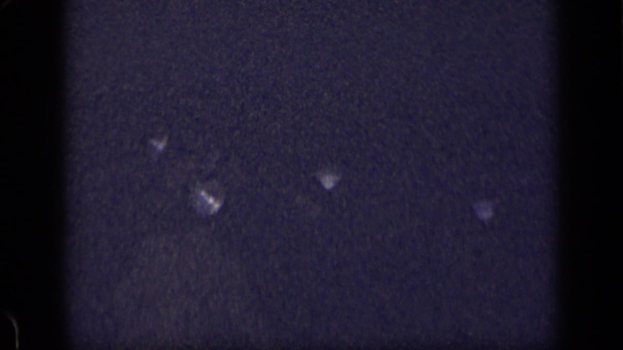 Dark grainy frame with vertical film edges and small pale reflective specks.