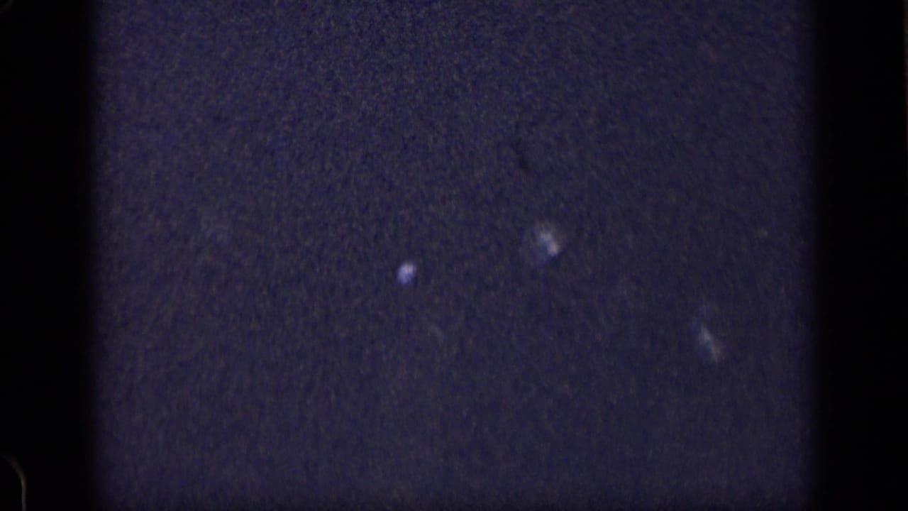 Dark grainy frame with a central black strip and scattered small light spots.