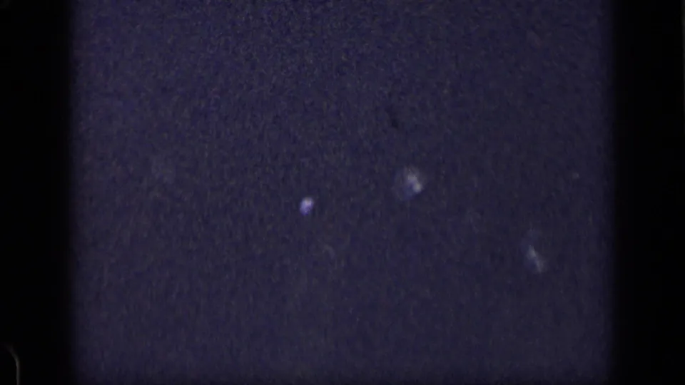 Dark 1957 New York 8mm frame showing a black vertical gate area, faint blue-black texture, and several small reflective points.