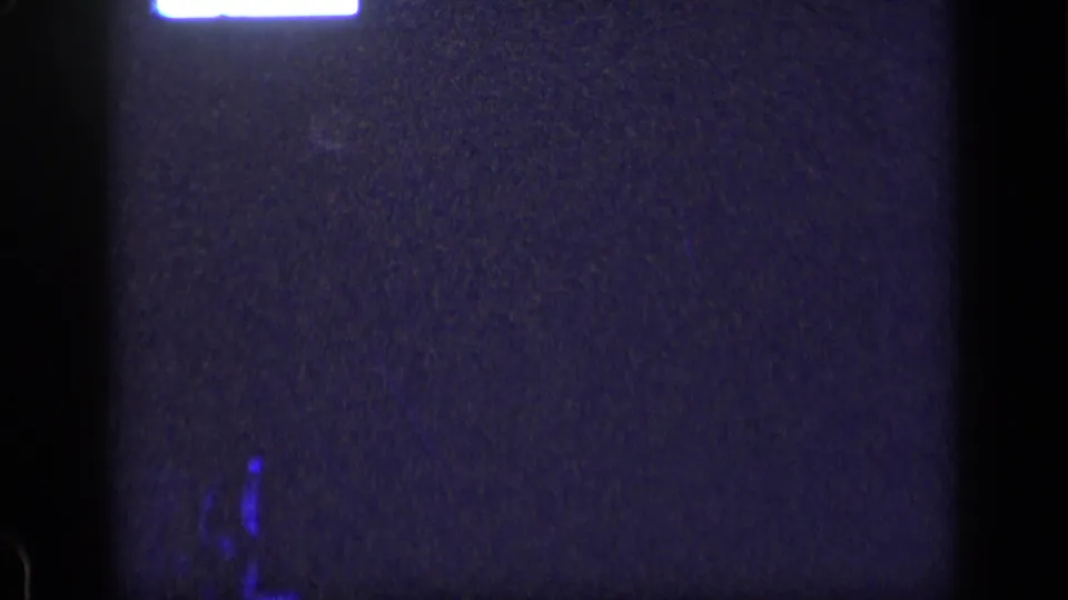 1957 New York 8mm frame showing an indistinct dark screen area with a bright top glow, blue artifacts, grain, and heavy vignetting.