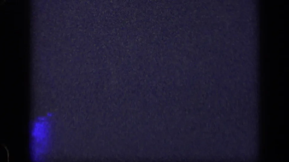 1957 New York 8mm frame with an indistinct dark surface, vivid blue lower glow, vignetting, and heavy film grain.
