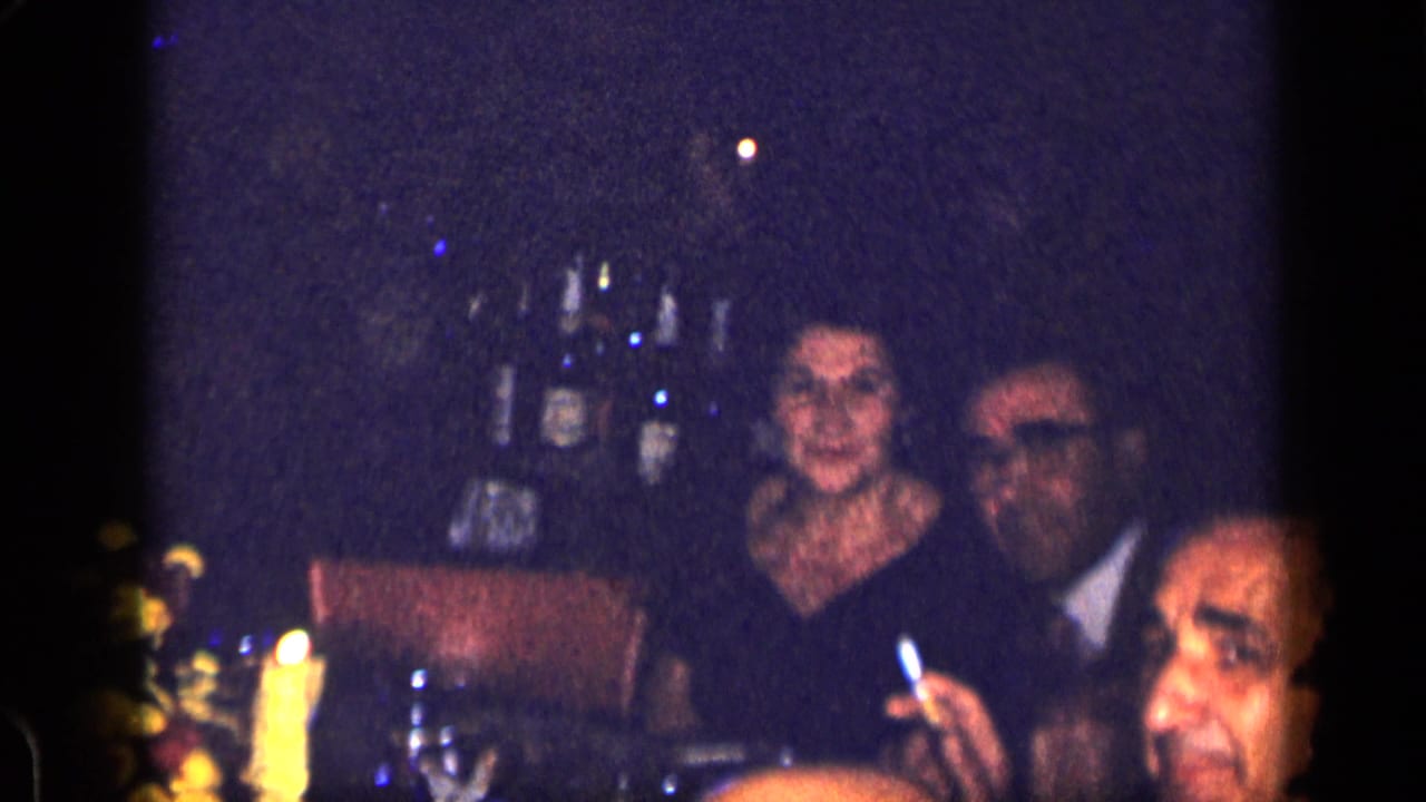 Woman and suited man sit at a candlelit table while another guest is cropped at right.