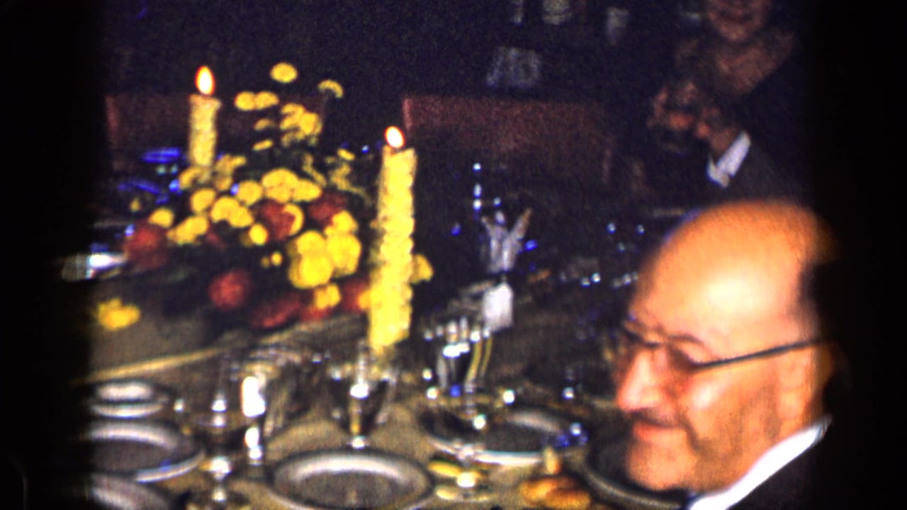 Candlelit dinner table with floral centerpieces and a seated man in formal attire.