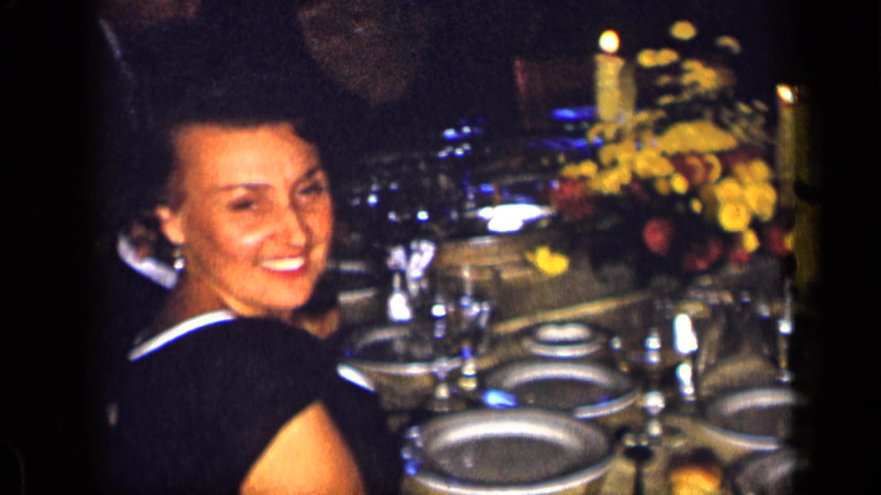 Smiling woman seated beside a formal table with candles, flowers, plates, and glasses.