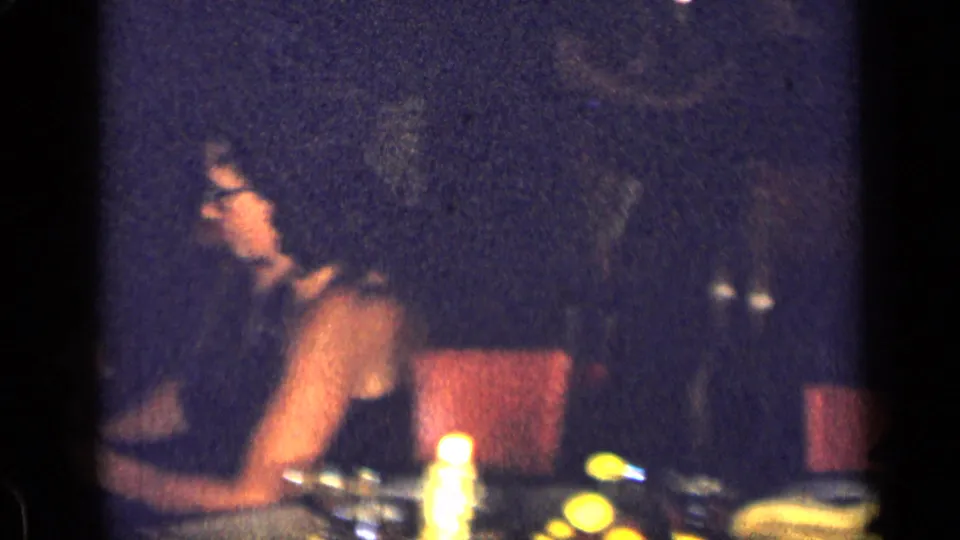 1957 New York dinner-party frame showing a woman seated at a candlelit table with plates and glassware nearby.