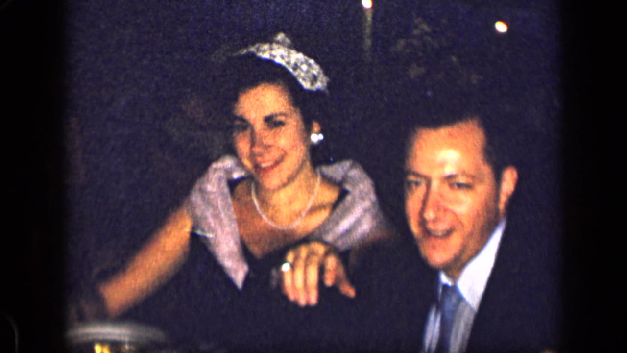 1957 New York formal event frame with a smiling crowned woman beside a formally dressed man.