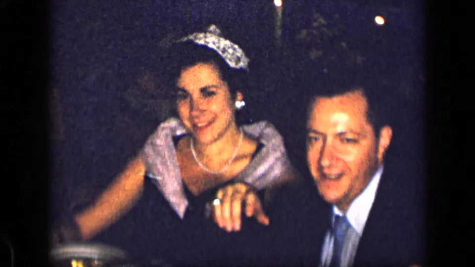 1957 New York formal event frame with a smiling crowned woman beside a formally dressed man.
