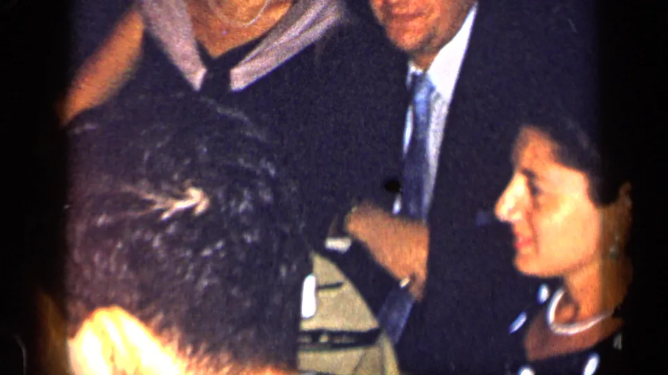 1957 New York home-movie frame showing formally dressed adults gathered around a table.