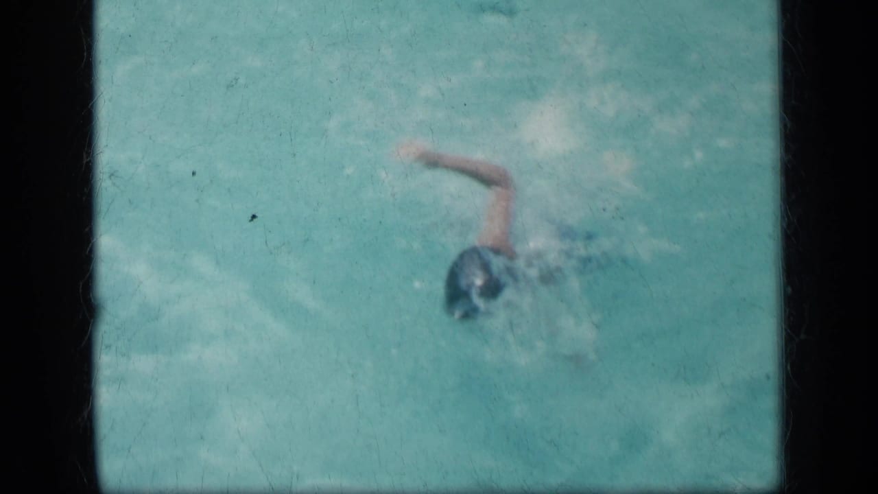Child in a dark swim cap swimming through turquoise pool water.