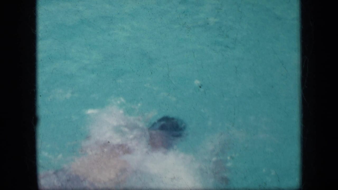 Swimmer in a turquoise pool with splashing water and black film borders.