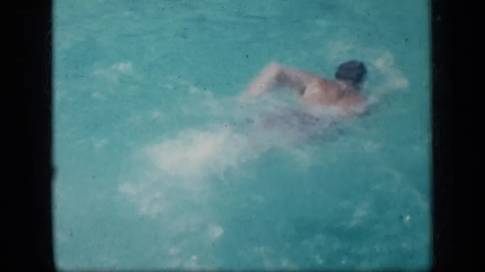 A swimmer crosses the turquoise pool in a 1957 New York home movie, with arms and shoulders visible above the water.