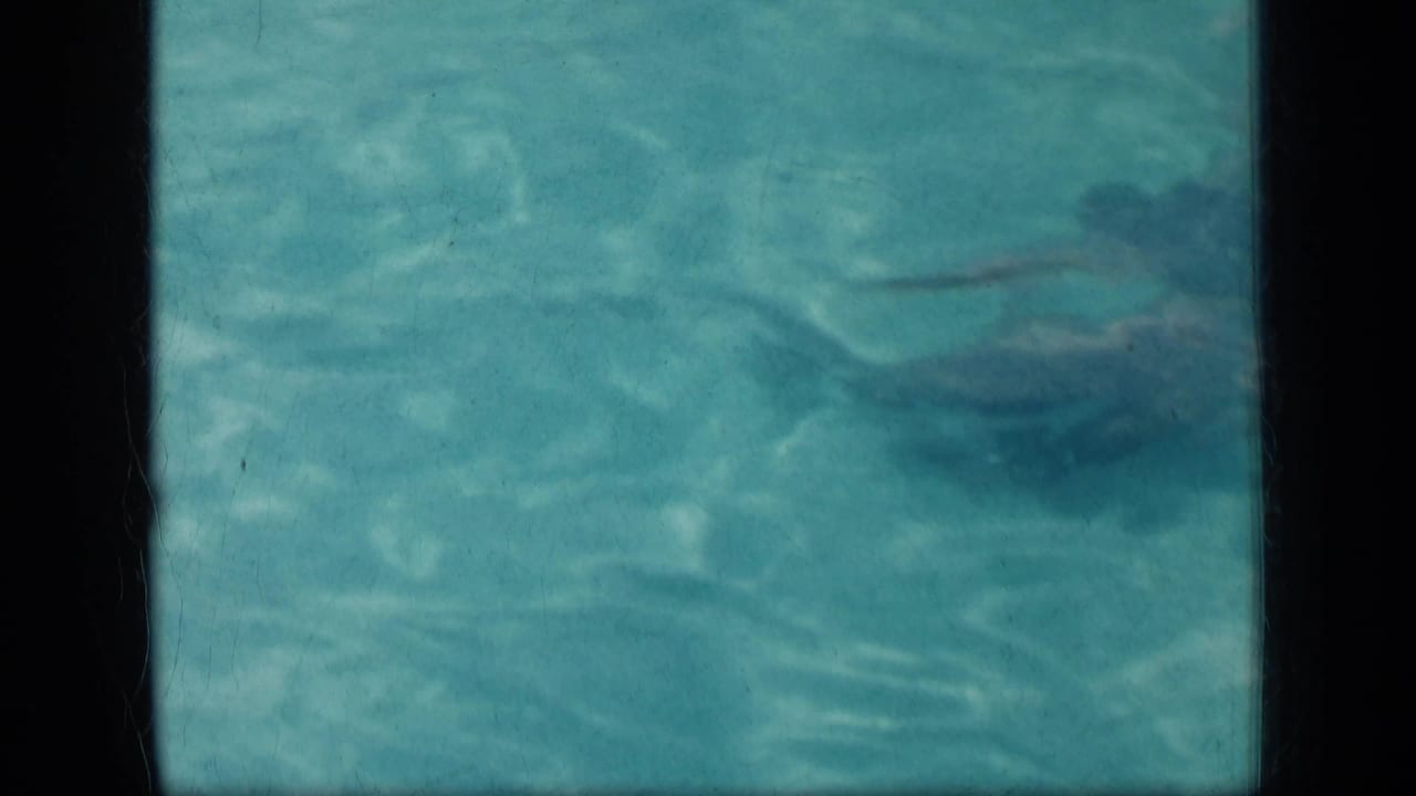 Swimmer's body appears near the top right under rippling pool water.