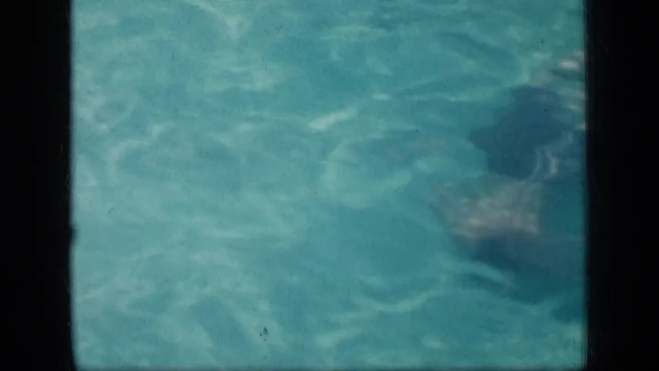 1957 New York home-movie frame showing a swimmer in dark trunks moving through a public pool.