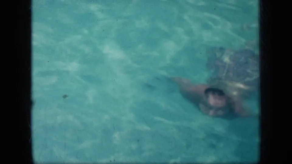 1957 New York 8mm frame with a man's face briefly visible as he swims across a public pool.