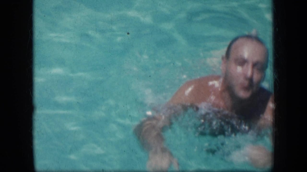 Man surfaces in a turquoise swimming pool, seen through dark film frame borders.
