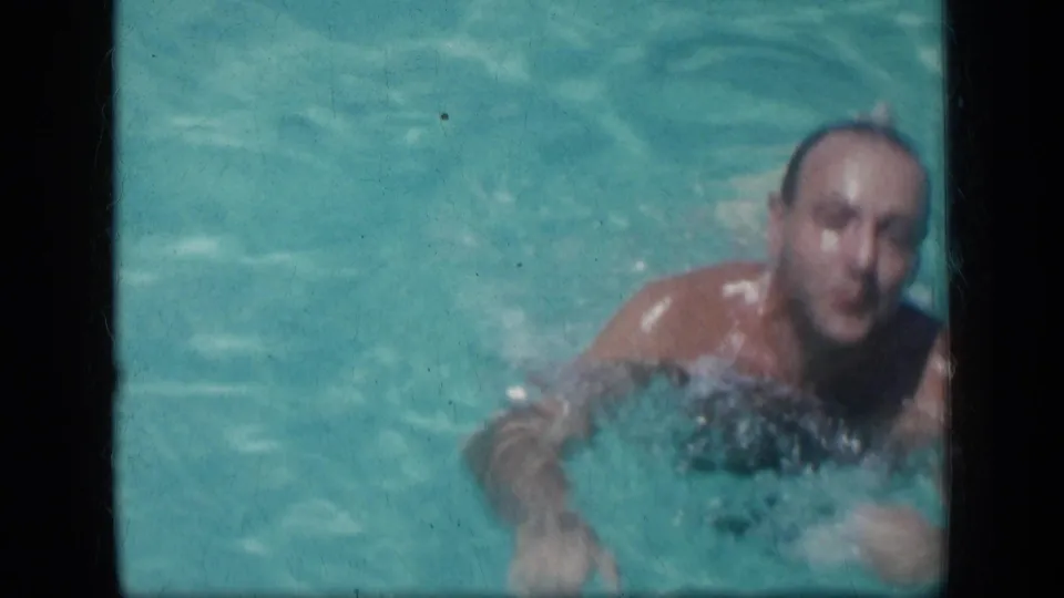 In 1957 New York home-movie footage, a man swims toward the camera in a turquoise pool as water ripples around him.