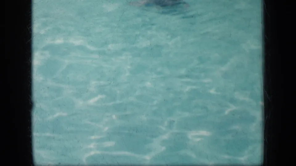 A nearly empty pool view shows rippling turquoise water within the dark borders of the scanned 8mm home-movie frame.