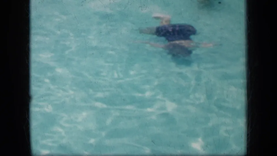 Another swimmer, likely an adult, moves through the turquoise pool water in the 1957 New York home-movie footage.