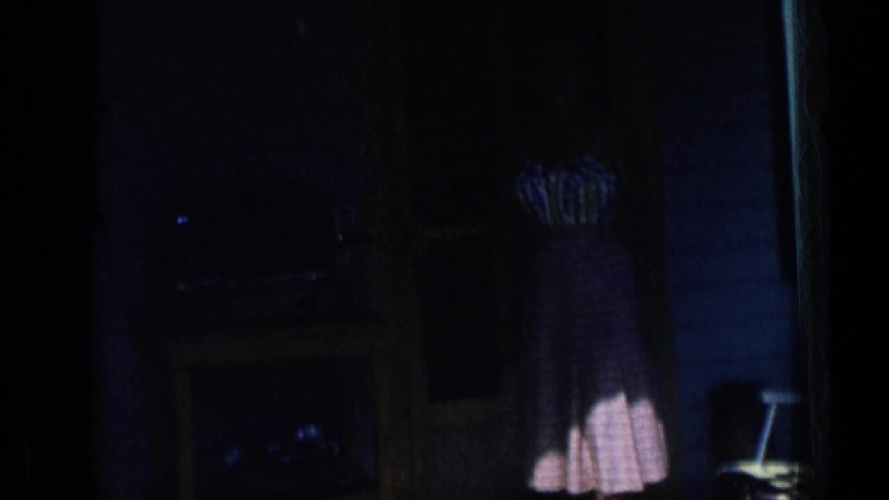 Dim interior doorway with a woman partly visible in a 1950s-style dress near a porch opening.