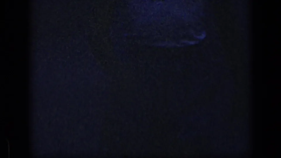 Underexposed 1957 New York 8mm frame with a barely visible person shape in a dark interior and strong film grain.