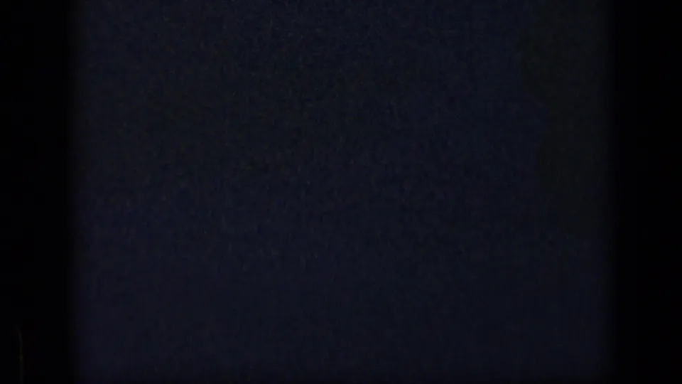 Dark scanned 8mm frame from the start of the 1957 New York clip, with grain and faint blue light marks.