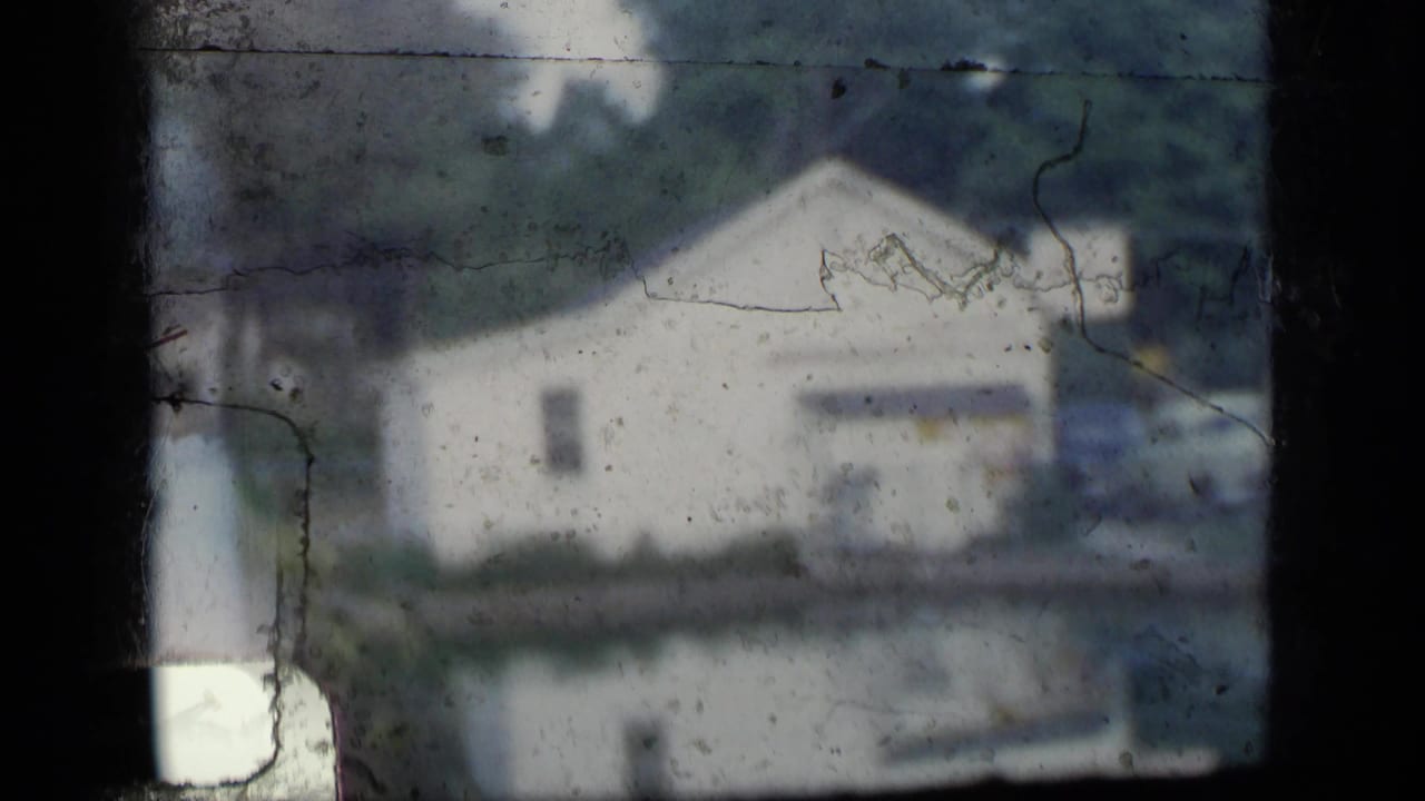 1957 New York aerial home-movie view of a pale waterfront building, trees, and reflected water, partially obscured by dark framing.