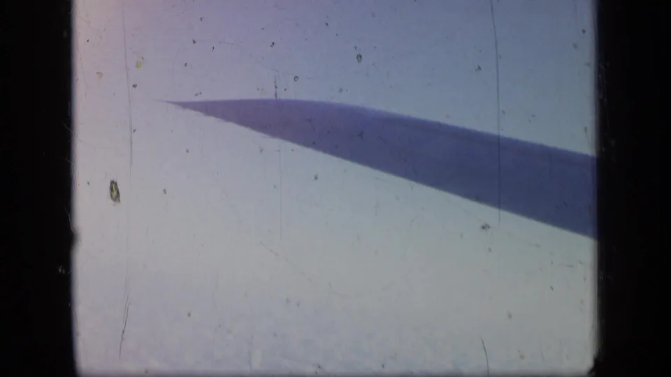 A steady 1957 airplane-window view shows the wing against pale sky and clouds, with 8mm dust and scratches.