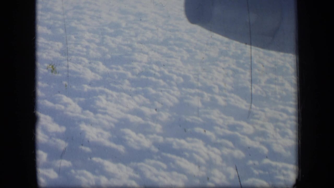 Cloud cover seen through a dark airplane window frame.