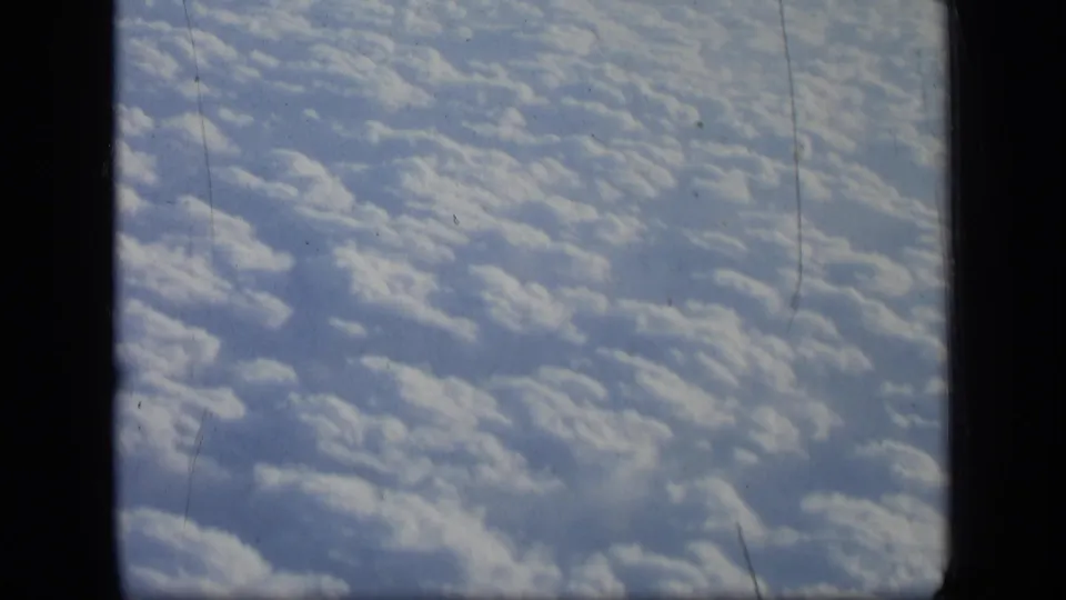 1957 8mm airplane-window view with textured cloud cover, dark framing, and visible film wear across the frame.
