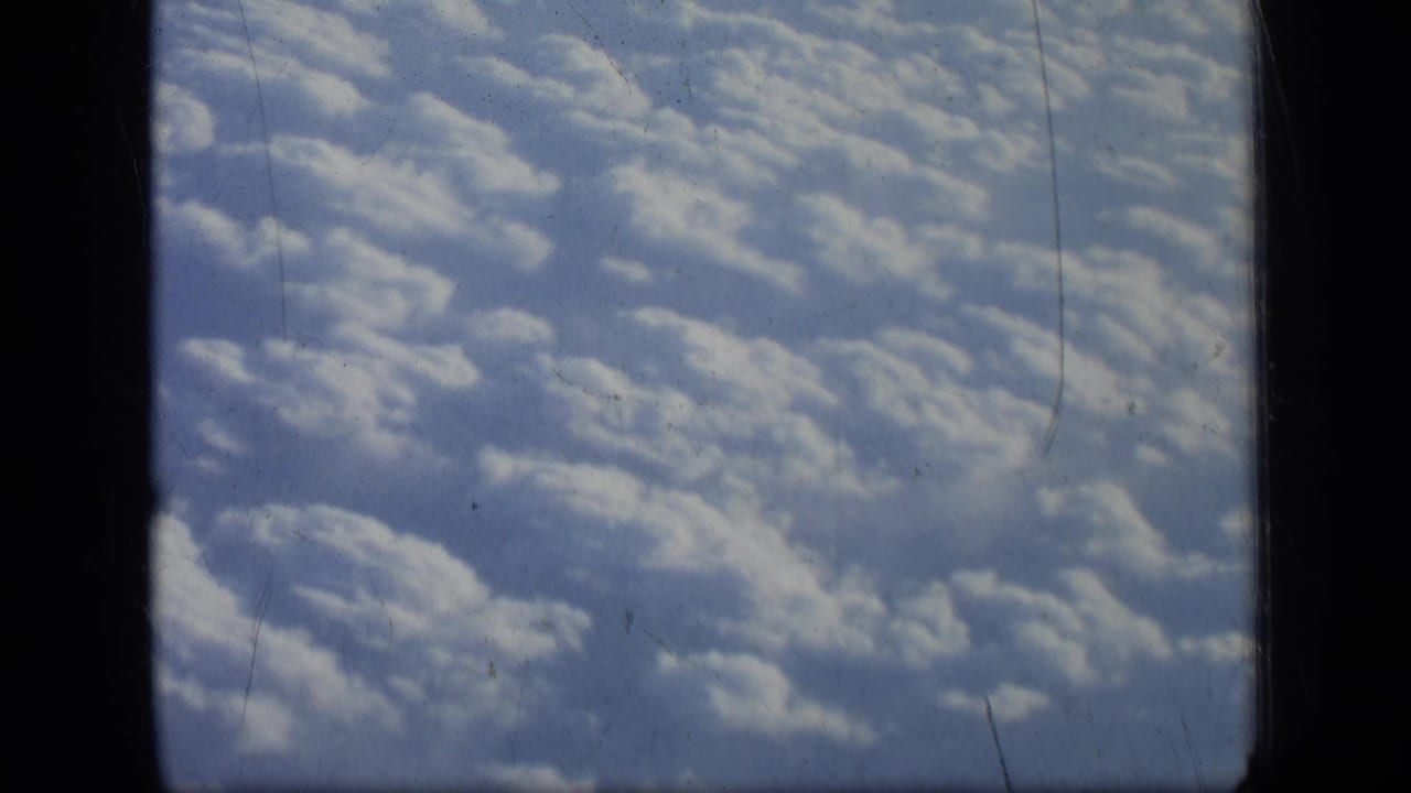 Scattered white clouds seen from above through a dark airplane window frame.