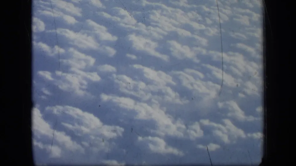 1957 8mm home-movie view of sunlit clouds from an airplane window, with dark film gate edges visible.
