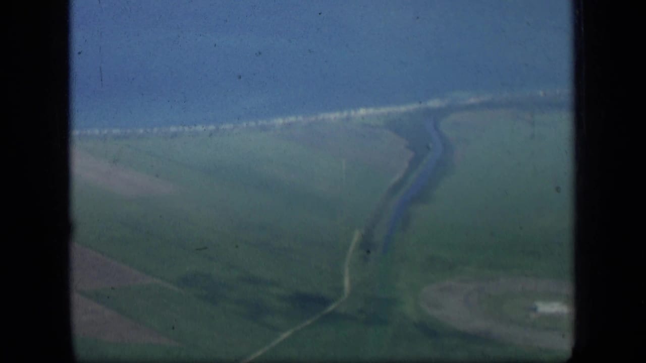 Aerial view of green fields, shoreline, and a winding waterway below.