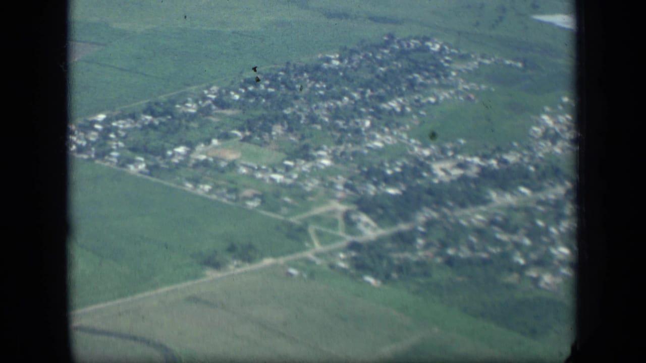 Aerial view of a compact town surrounded by green fields, framed by dark airplane window edges.