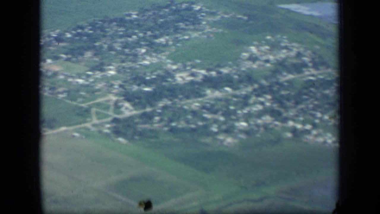 Aerial view of houses, roads, and surrounding fields seen through a dark window frame.