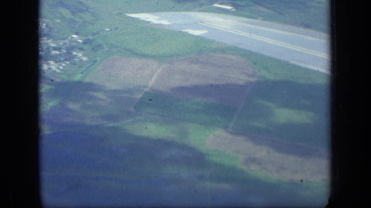 Aerial view of patchwork farmland and a long runway, framed by dark vertical film borders.