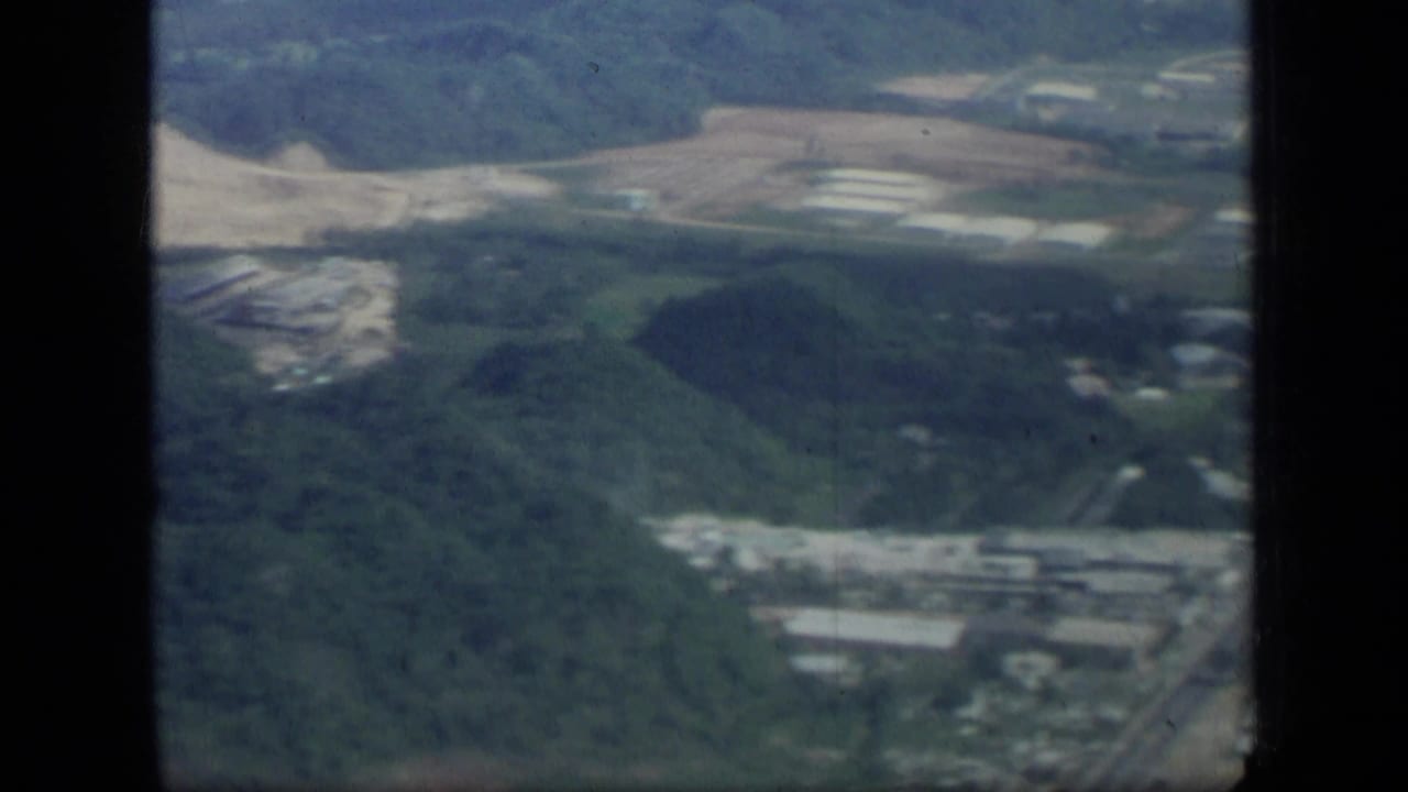 Aerial view of wooded hills, roads, light industrial buildings, and cleared ground.