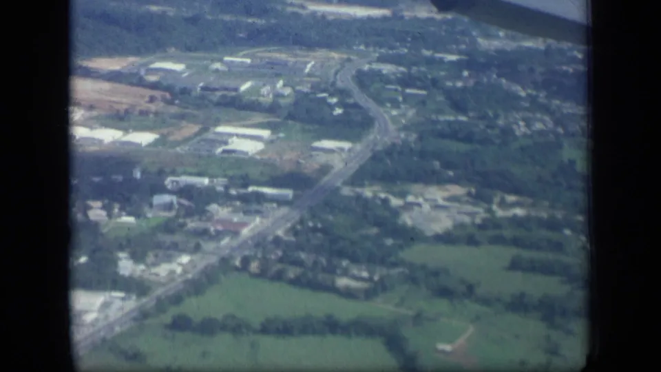 1957 New York aerial view of farmland and wooded areas with roads and scattered low buildings visible below.
