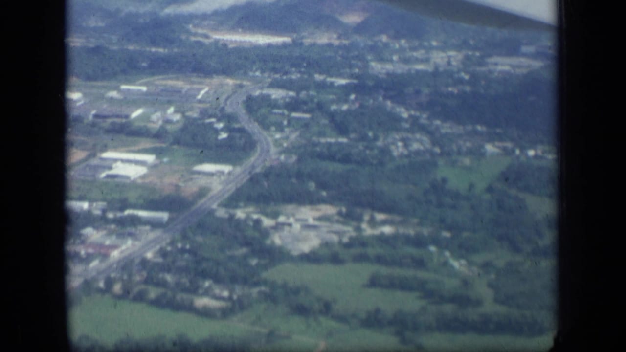 Aerial view of green fields, roads, and scattered buildings seen through an airplane window.