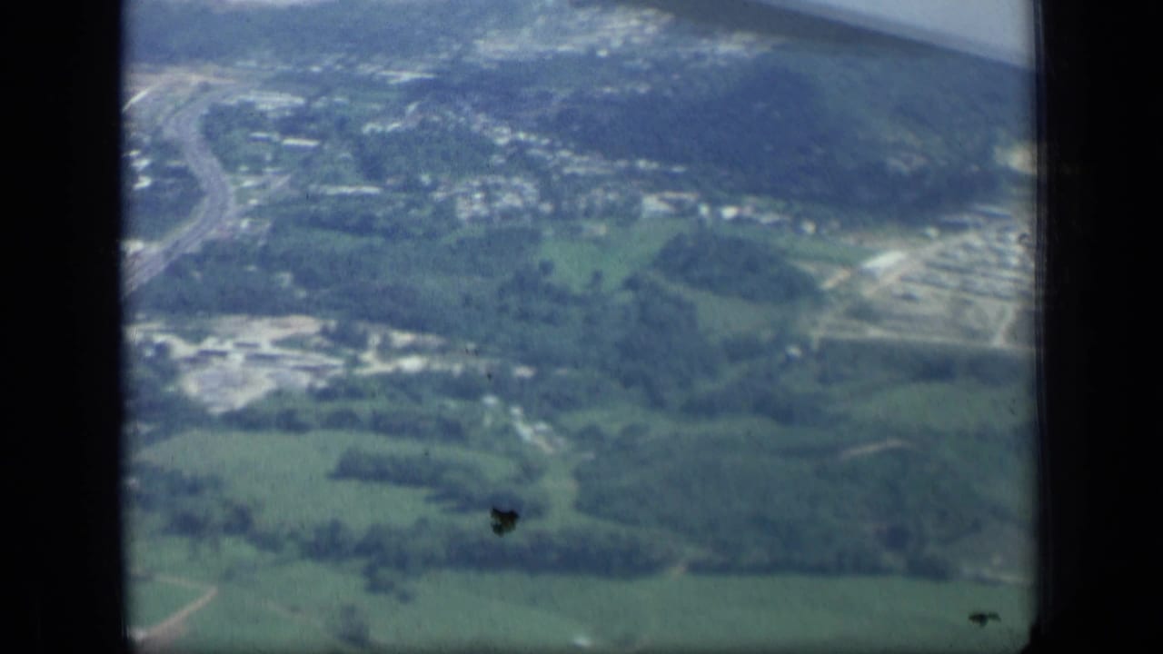 Aerial landscape with fields, roads, wooded areas, and scattered buildings through an aircraft window.