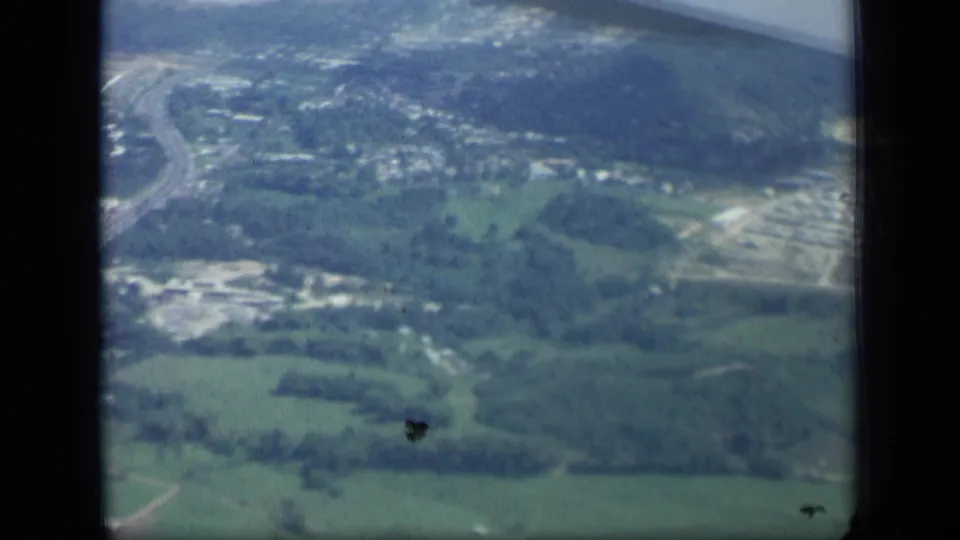 1957 New York aerial home-movie view of rural and small-town terrain, with roads and buildings visible beyond the airplane window frame.