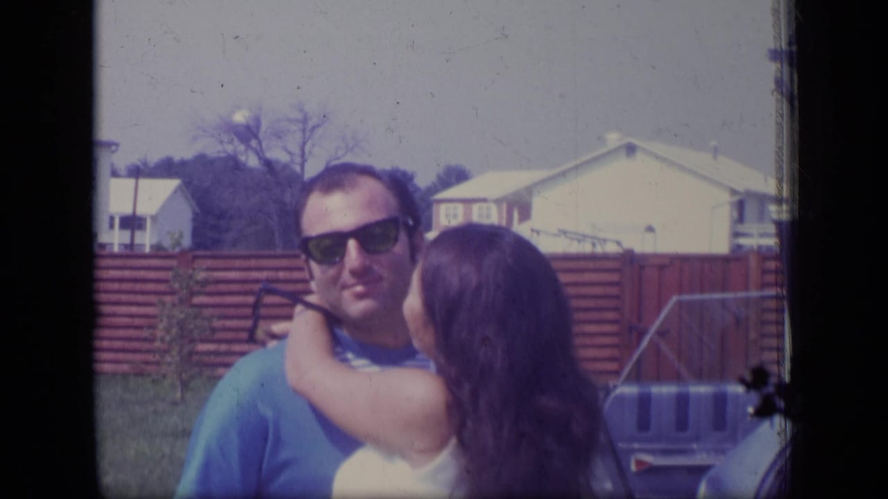 Woman kisses or embraces a man in sunglasses in a backyard.