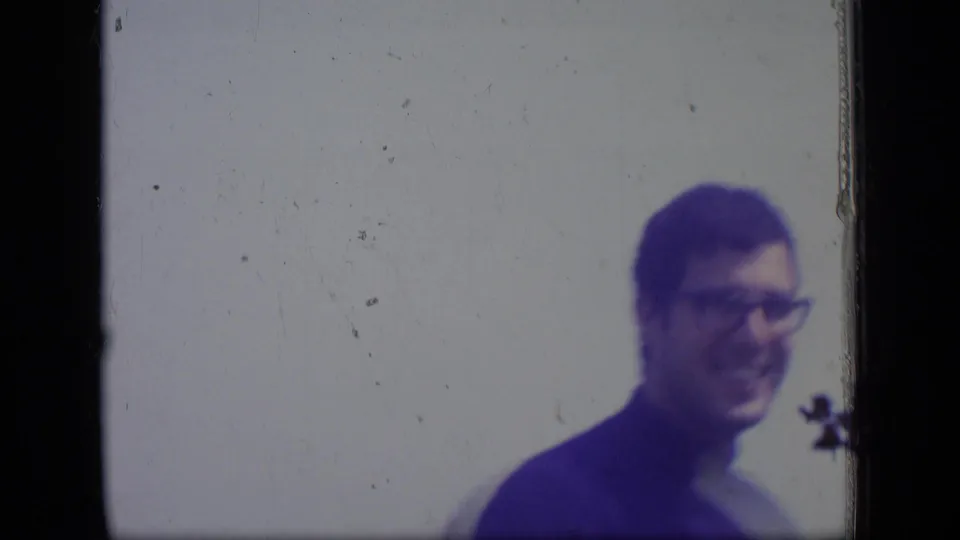 At the end of the clip, the man appears blurred and partly to the right of frame against a pale outdoor background.