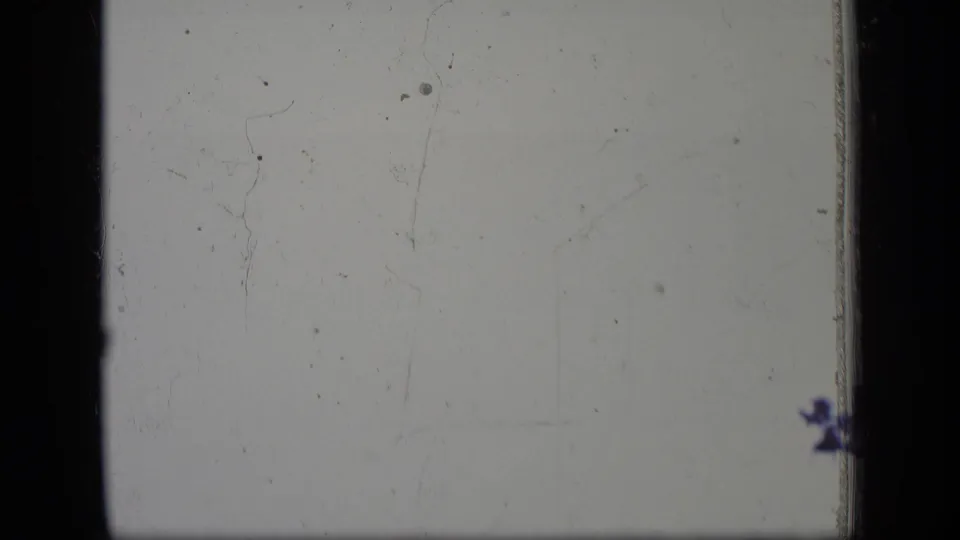 End frame from the 8mm scan with a pale exposed area, scratches, dust specks and dark film borders, with no clear people visible.
