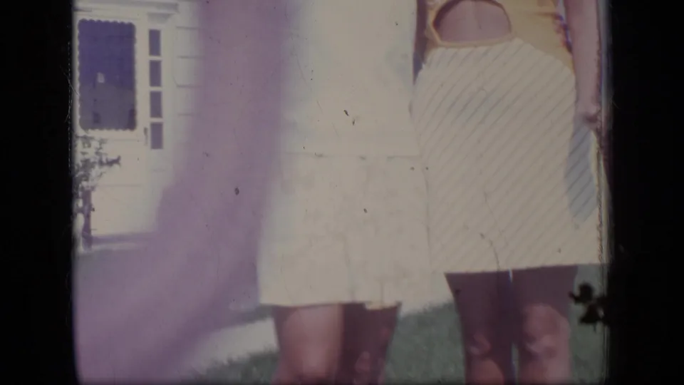 A close crop shows the women's summer dresses, with the house entrance and lawn partially visible in the background.