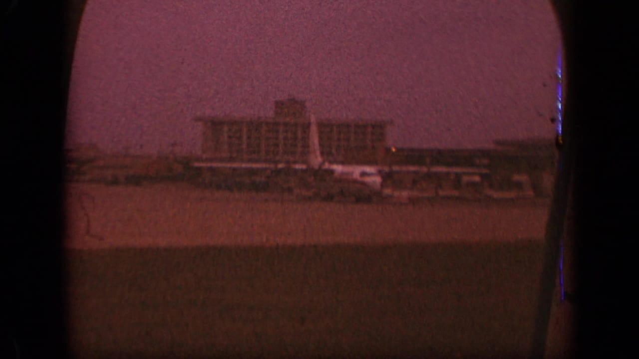 Terminal building and tarmac seen through dark airplane-window edges.